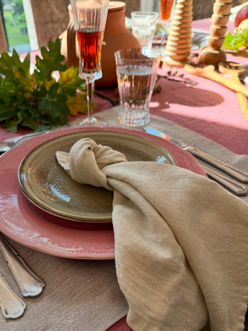 Sfeervol gedekte herfsttafel met oudroze tafellinnen, naturel linnen placemat en servet, gecombineerd met roze en aardewerken servies. Glazen, zilverkleurig bestek, herfstbladeren en houten kandelaars zorgen voor een warme, Toscaanse sfeer.